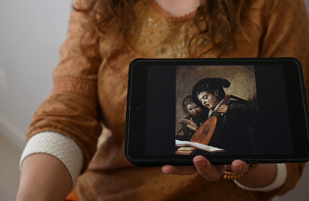 Juf met iPad en foto van schilderij van Frans Hals (Twee zingende jongens)