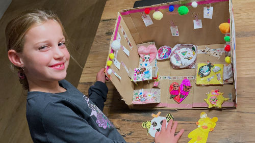 Meisje die een poppenhuis heeft gemaakt van karton